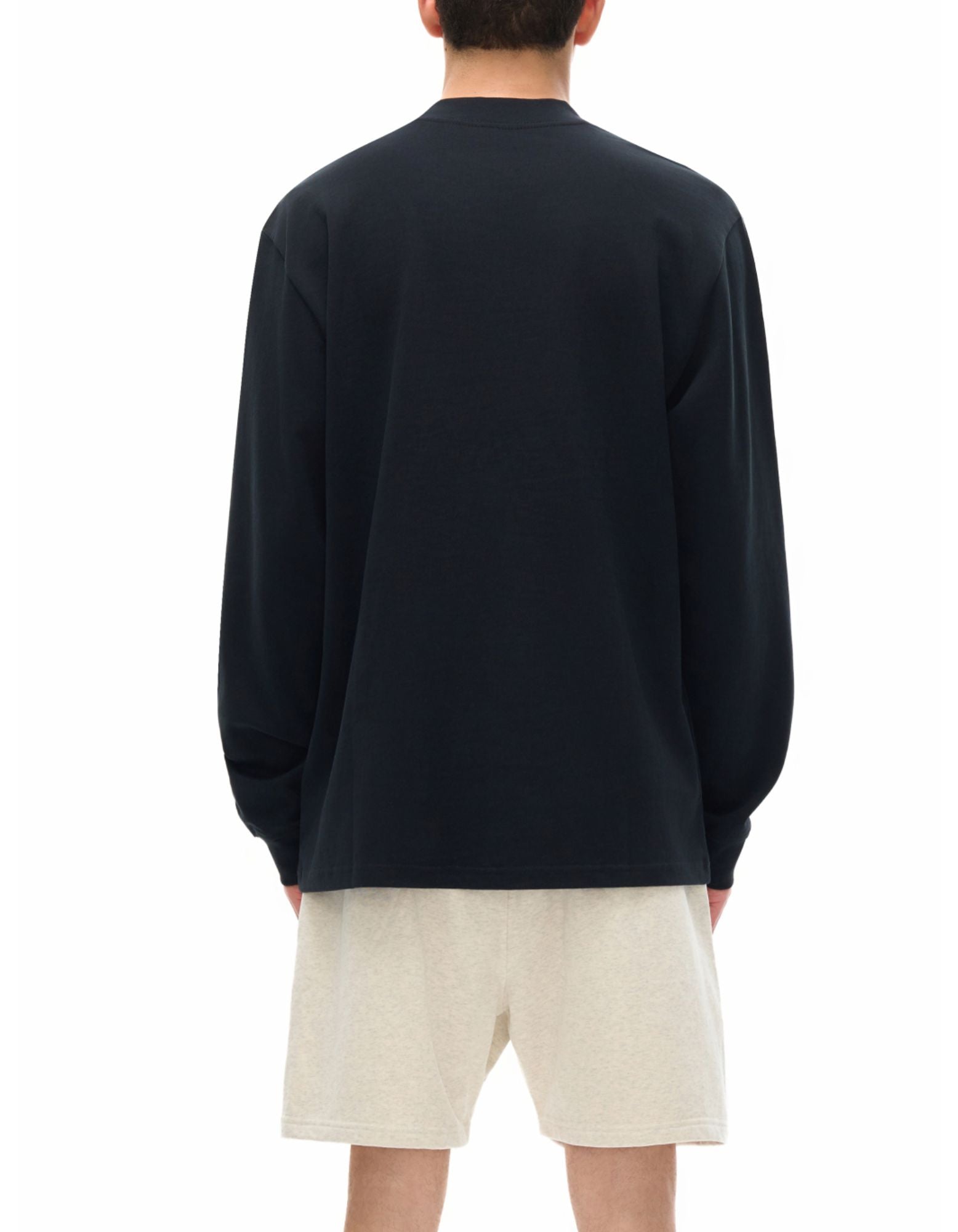 Person wearing a black long sleeve t-shirt and beige shorts on a white background